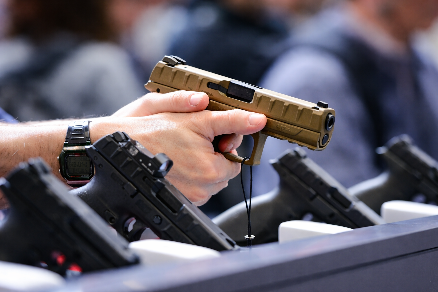 Person holding a tan handgun, with other black handguns on display.