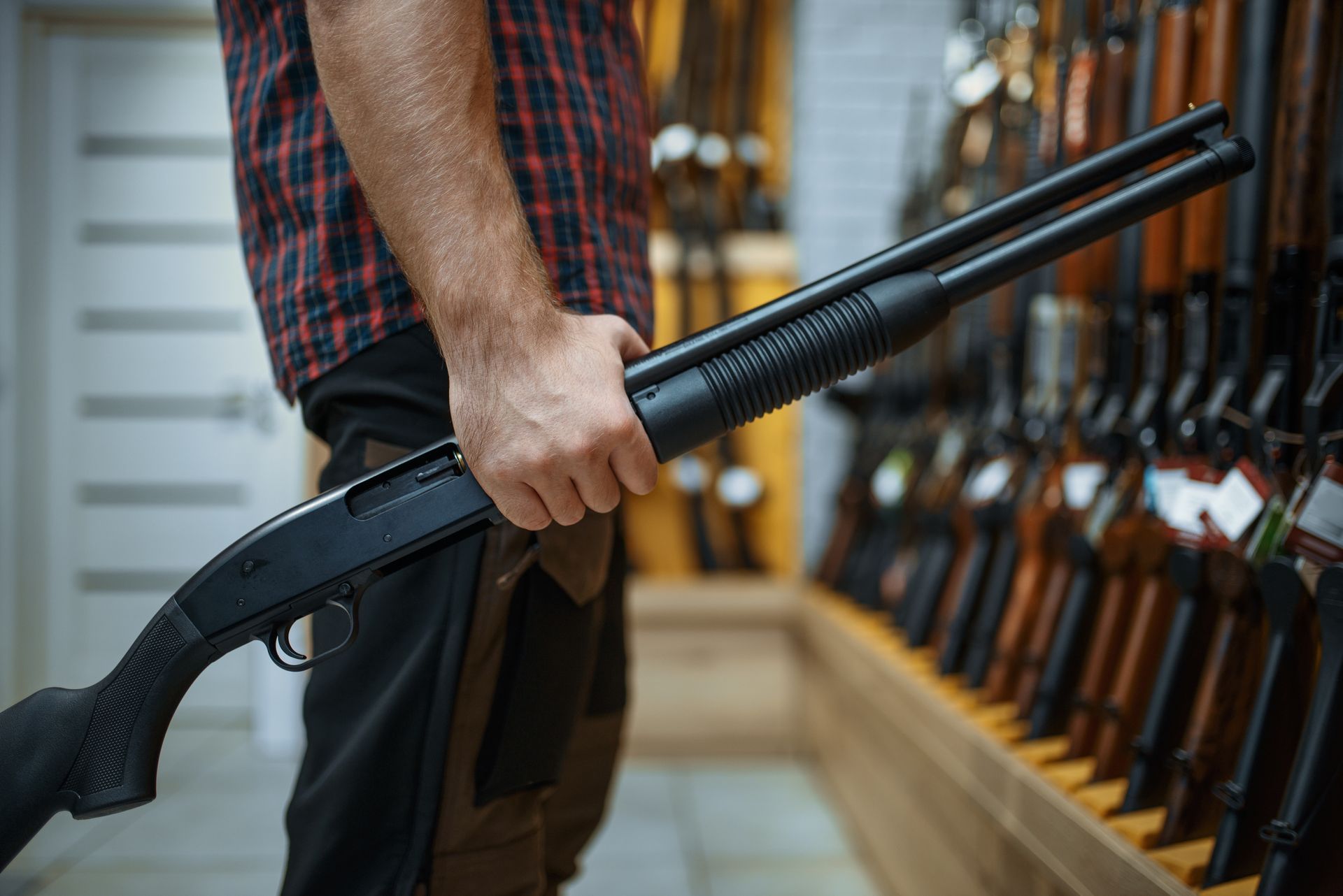 Person holding a black shotgun in a gun store, with rifles on display in the background.